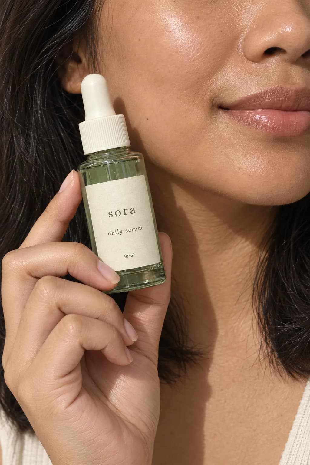 Model memegang serum Sora hijau sage di dekat wajah