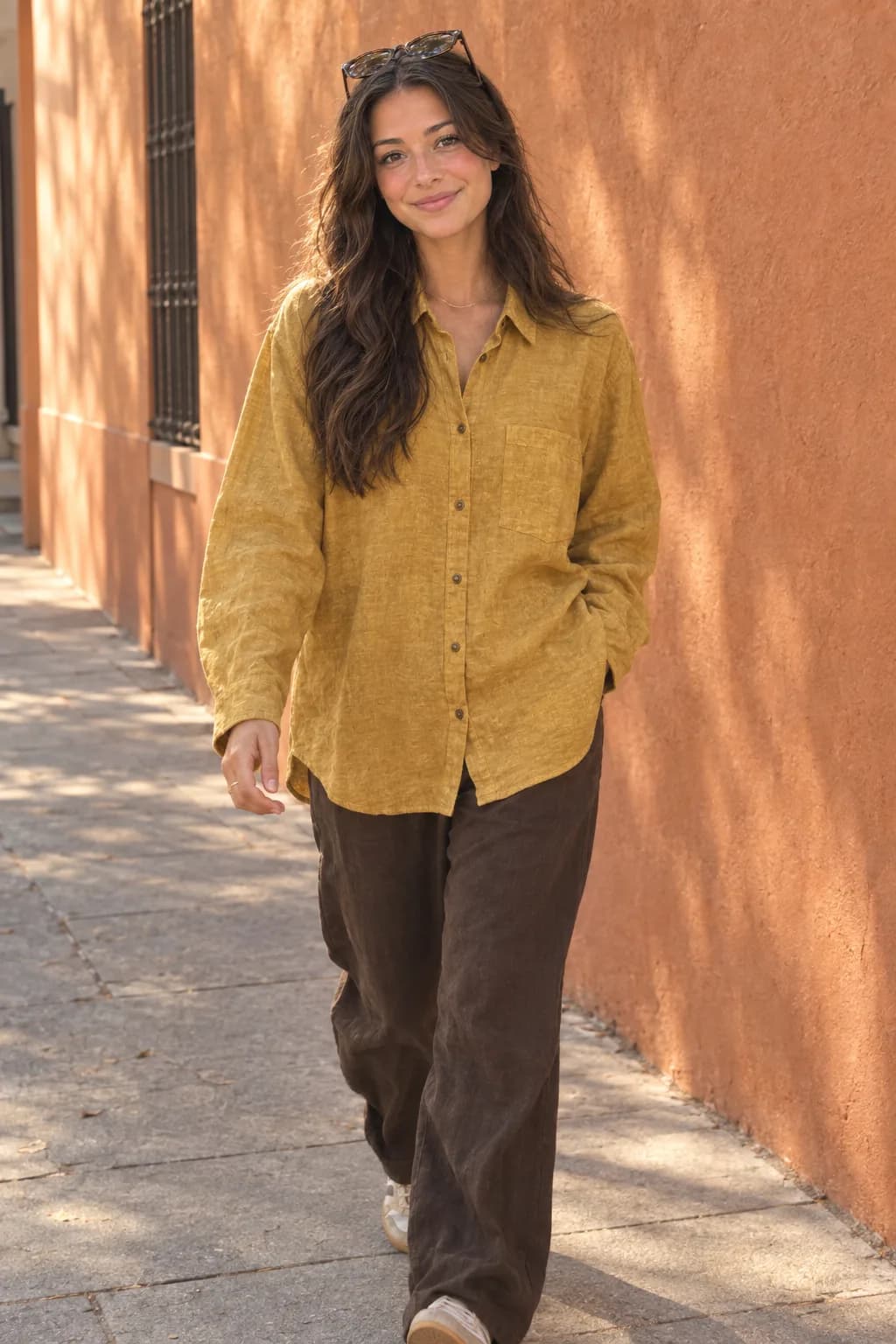 Model berjalan memakai kemeja linen mustard di luar ruangan
