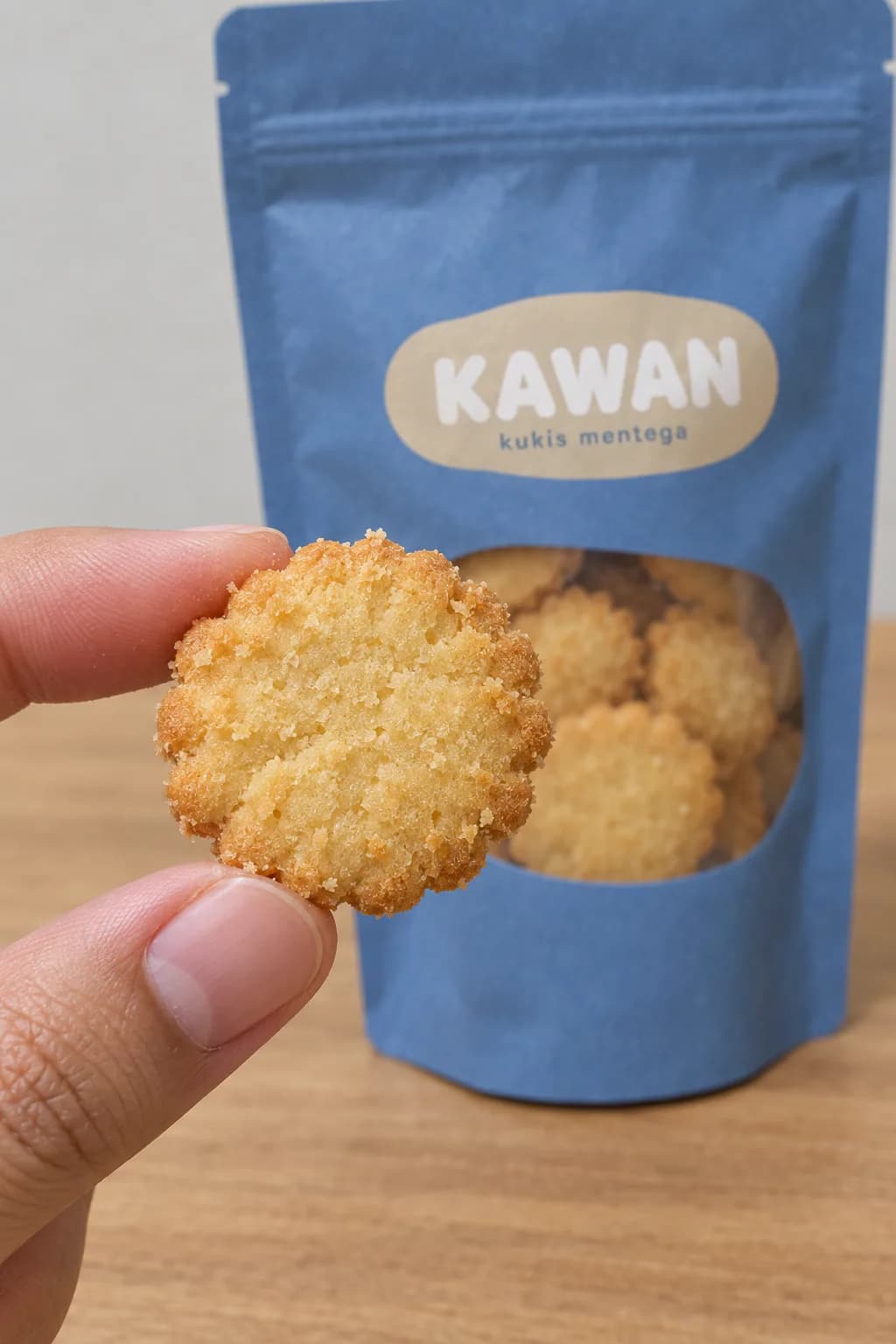 Satu kukis Kawan dipegang dua jari dengan kemasan di latar belakang