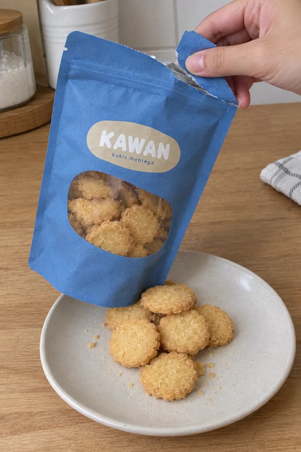 Tangan membuka kemasan kukis Kawan dengan kukis tertuang di piring